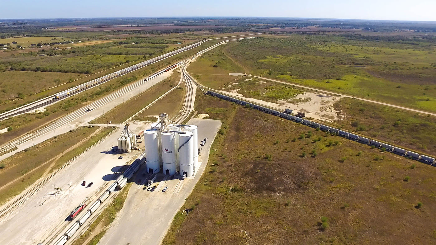 Aerial view of the Twin Eagle transload terminal: silos, loading pad and a string of railcars curving along the lead track