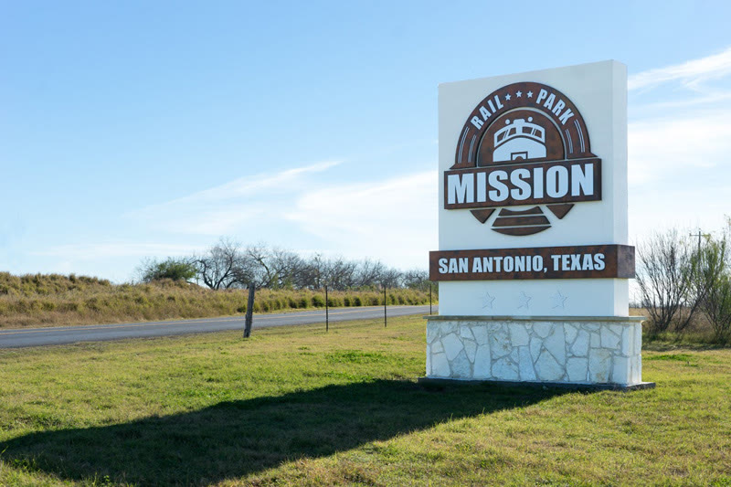 Stone monument sign reading Mission Rail Park, San Antonio, Texas at the park entrance